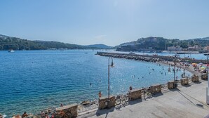 A coastal scene with a clear view of the sea, a stone pier, and a distant hill with buildings. - Sea view apartment in Porto Azzurro (Porto Azzurro)