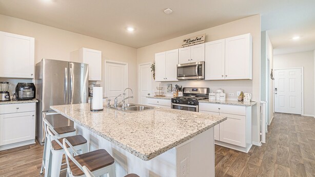 A modern kitchen with white cabinetry, granite countertops, stainless steel appliances, and a central island with bar stools.