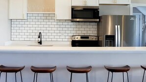 A modern kitchen with white cabinets, a black countertop, a stainless steel refrigerator, and three pendant lights. - Sojourn The Lighthouse  Beach Front Resort Villa (Norfolk)