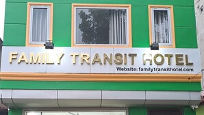 L’extérieur du Family Transit Hotel se caractérise par sa façade verte, un panneau indicateur et une entrée en verre.