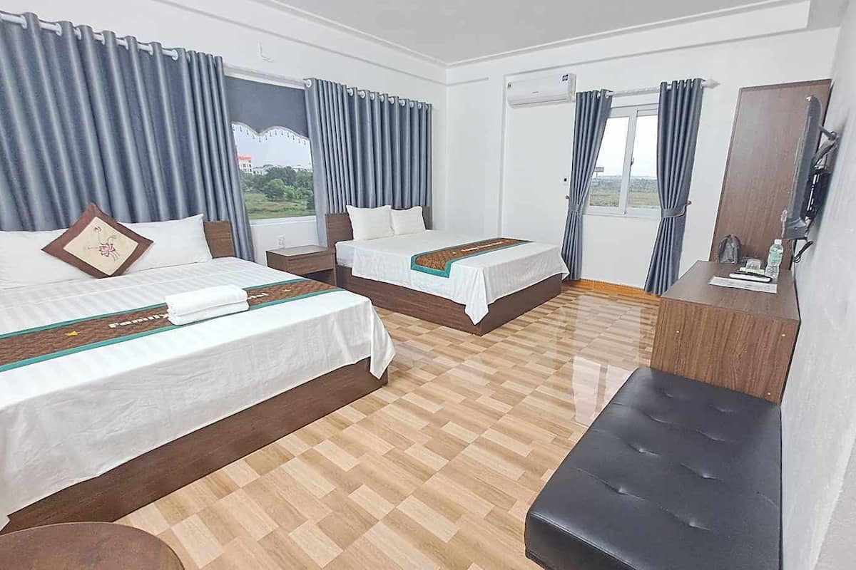 Ein Hotelzimmer mit zwei Betten, Holzboden, Schreibtisch und Blick auf Grünfläche.