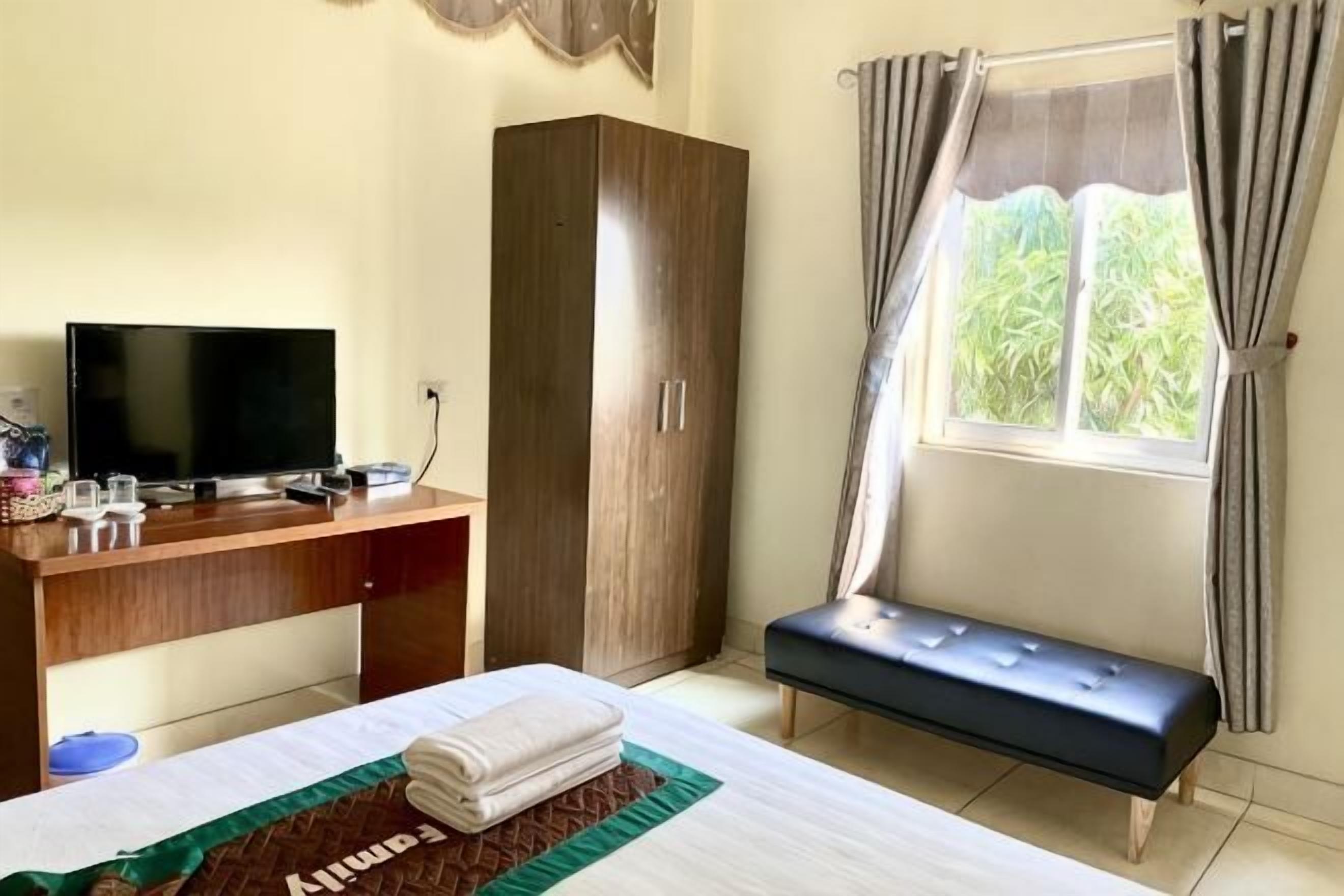 Een kamer met een bed, een bureau met een televisie, een kledingkast en een raam met gordijnen.