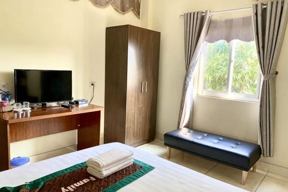Une chambre avec un lit, un bureau avec une télévision, une armoire et une fenêtre avec des rideaux.