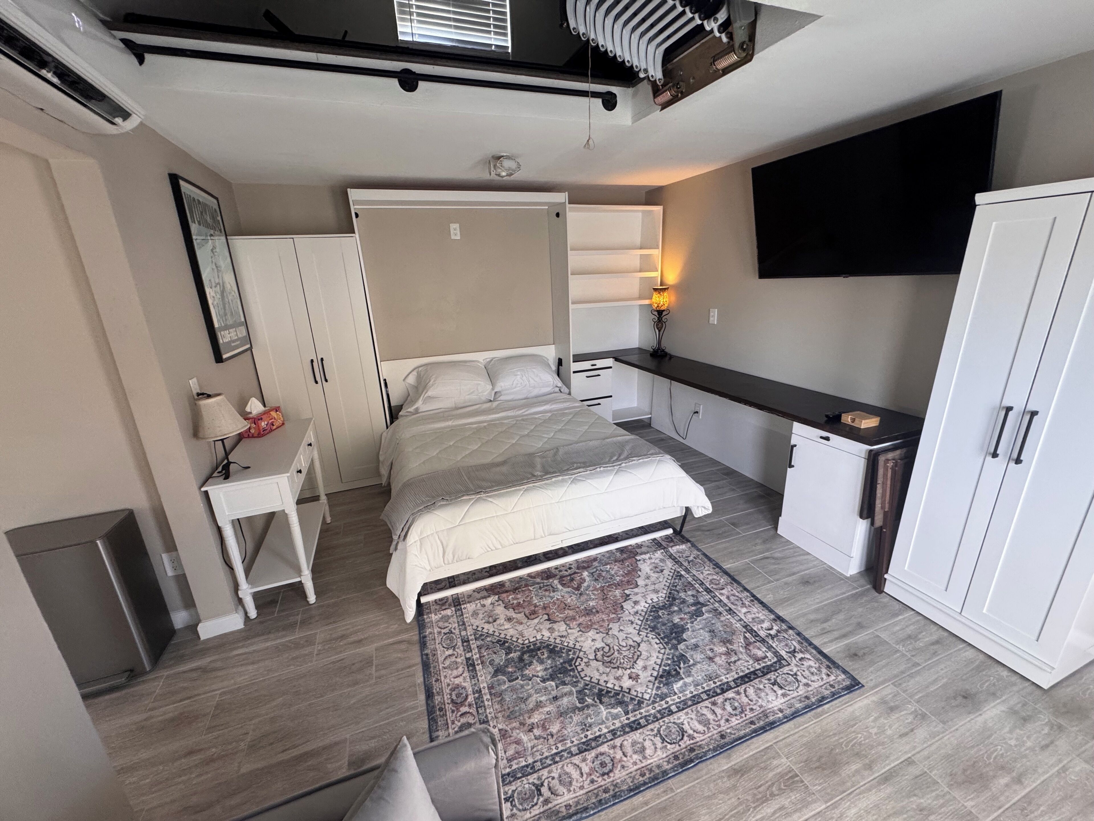 A bedroom with a bed, bedside table, lamp, wardrobe, and a TV mounted on the wall.