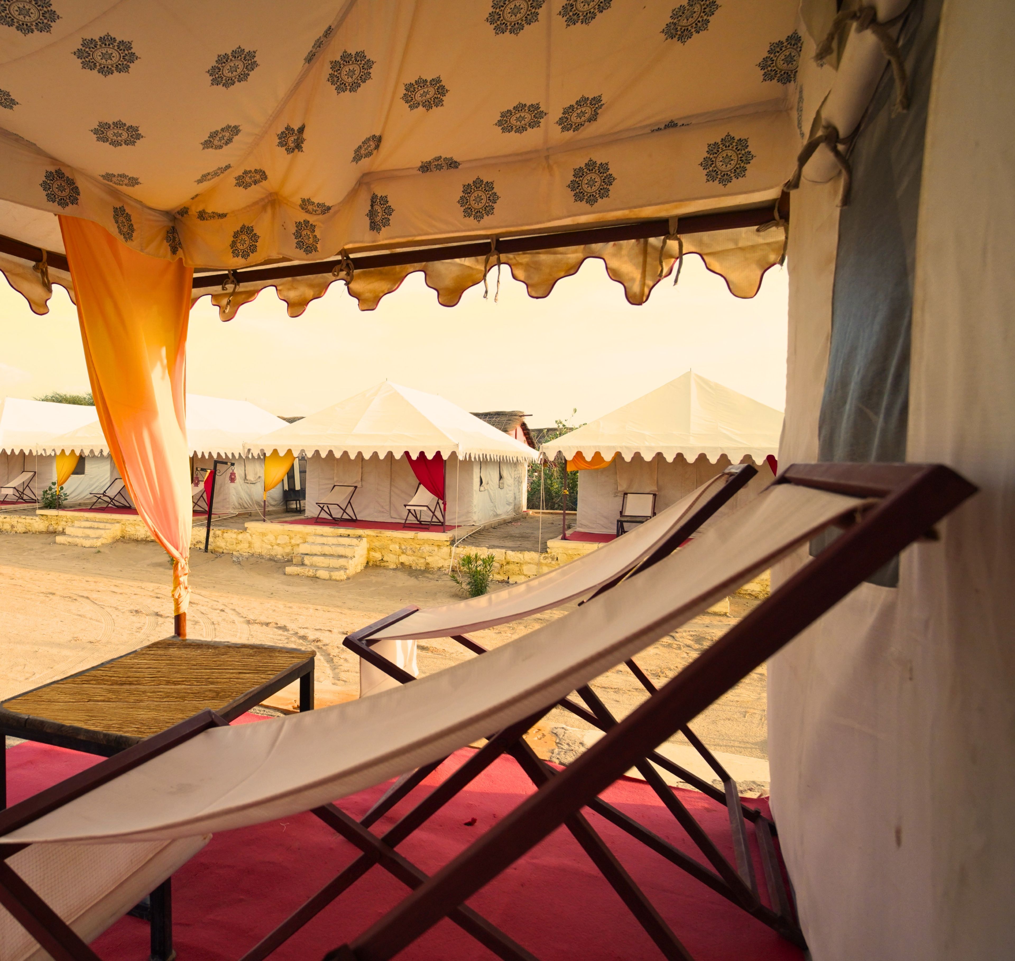 A tented area with a red carpet, a table, and two lounge chairs.