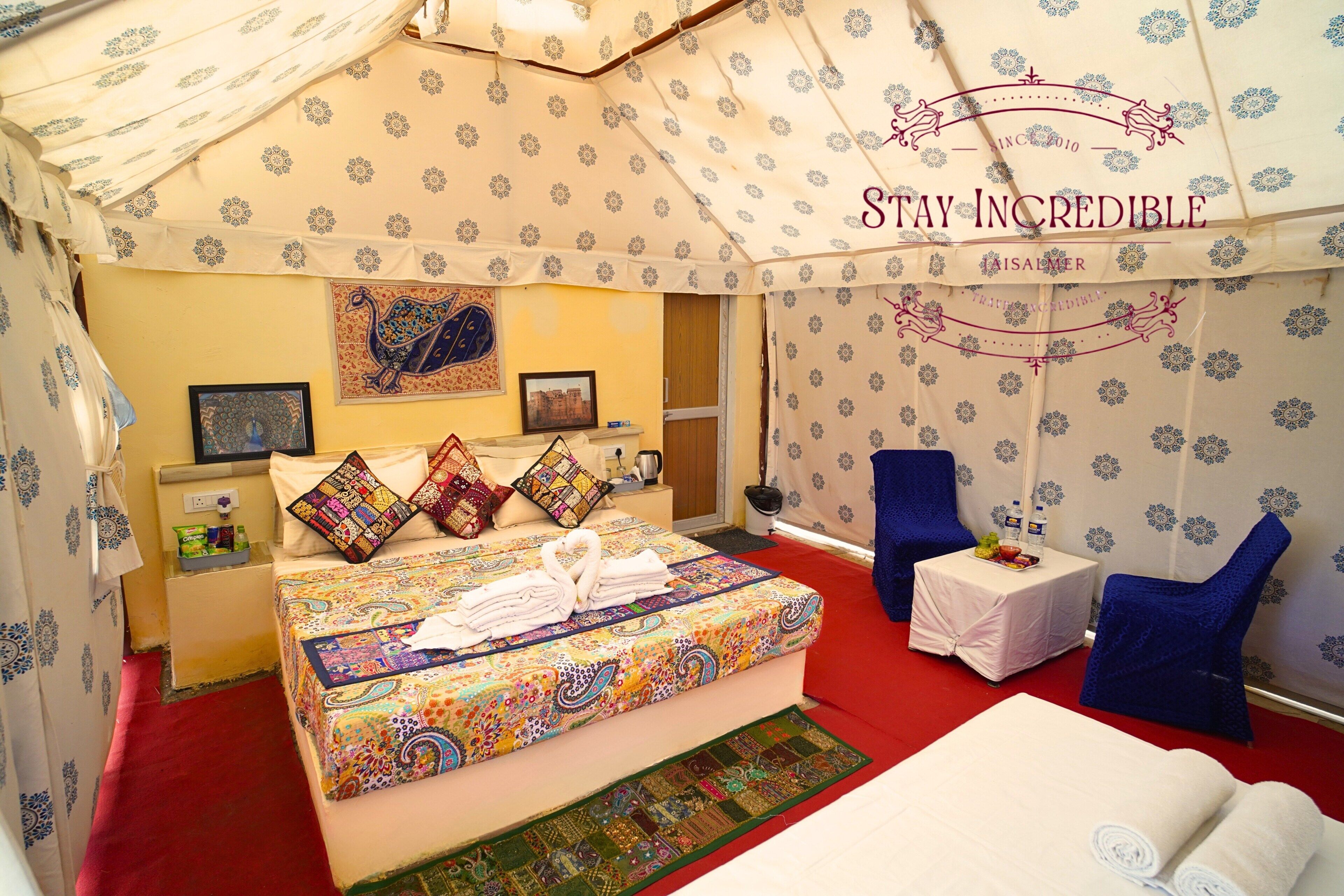 Quarto tipo tenda com cama, travesseiros, uma mesa pequena com bandeja e uma cadeira.
