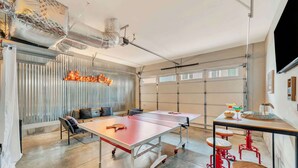 A ping pong table with stools, a seating area with cushions, and a large window with curtains. - Music-themed Nashville home sleeps 12 with ping pong game room, pet friendly (Nashville)