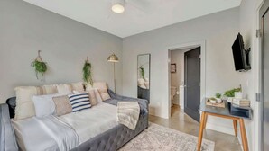 A modern bedroom with a tufted bed, a standing lamp, a flat-screen TV, and a small table with plants. - Music-themed Nashville home sleeps 12 with ping pong game room, pet friendly (Nashville)