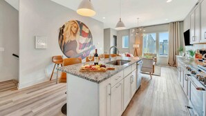 A modern kitchen with a central island, pendant lighting, and a large window providing natural light. - Music-themed Nashville home sleeps 12 with ping pong game room, pet friendly (Nashville)