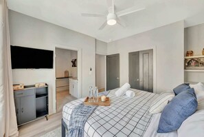 A modern bedroom with a bed, a TV, a wardrobe, and a ceiling fan.