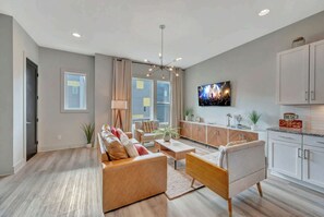 A modern living room with a sofa, coffee table, and TV. There is a kitchen area with cabinets and a countertop.