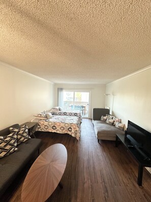 Una habitación moderna y bien iluminada con una cama, dos sofás, un televisor y una mesa de centro de madera.