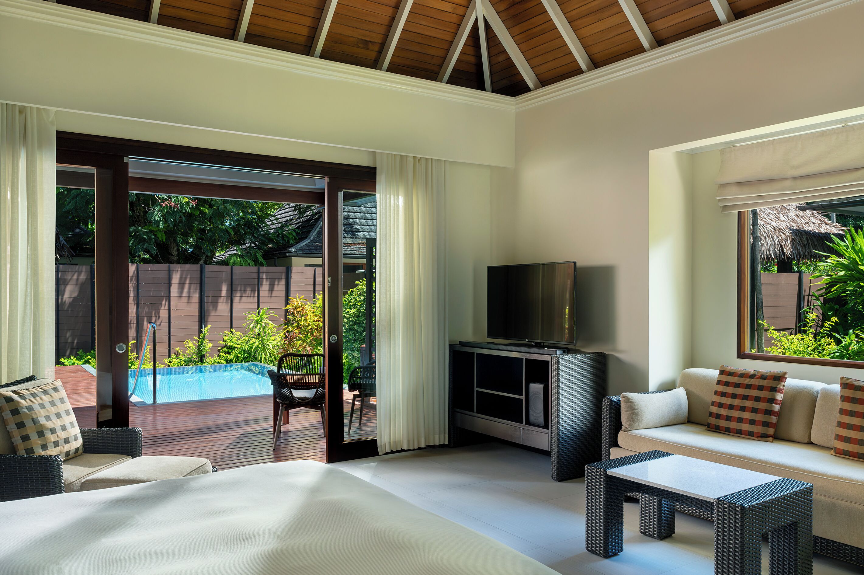 Una habitación de hotel moderna con una cama grande, un sofá, un televisor y vistas a una piscina y zonas verdes.