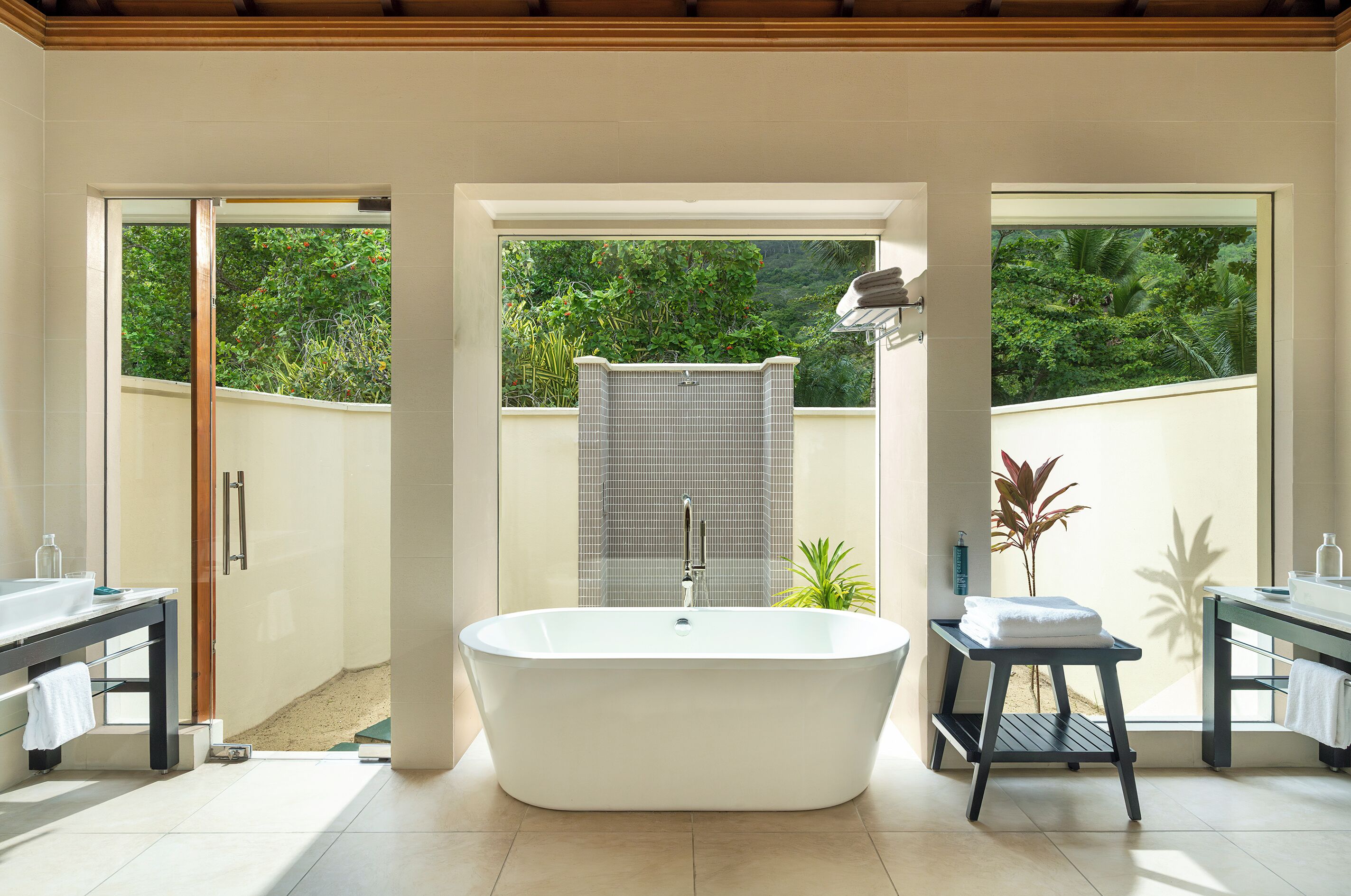 Un baño moderno con una bañera independiente, una ducha con cerramiento de vidrio y vistas a exuberante follaje a través de amplias ventanas.