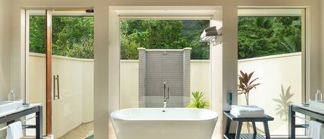 Un baño moderno con una bañera independiente, una ducha con cerramiento de vidrio y vistas a exuberante follaje a través de amplias ventanas.