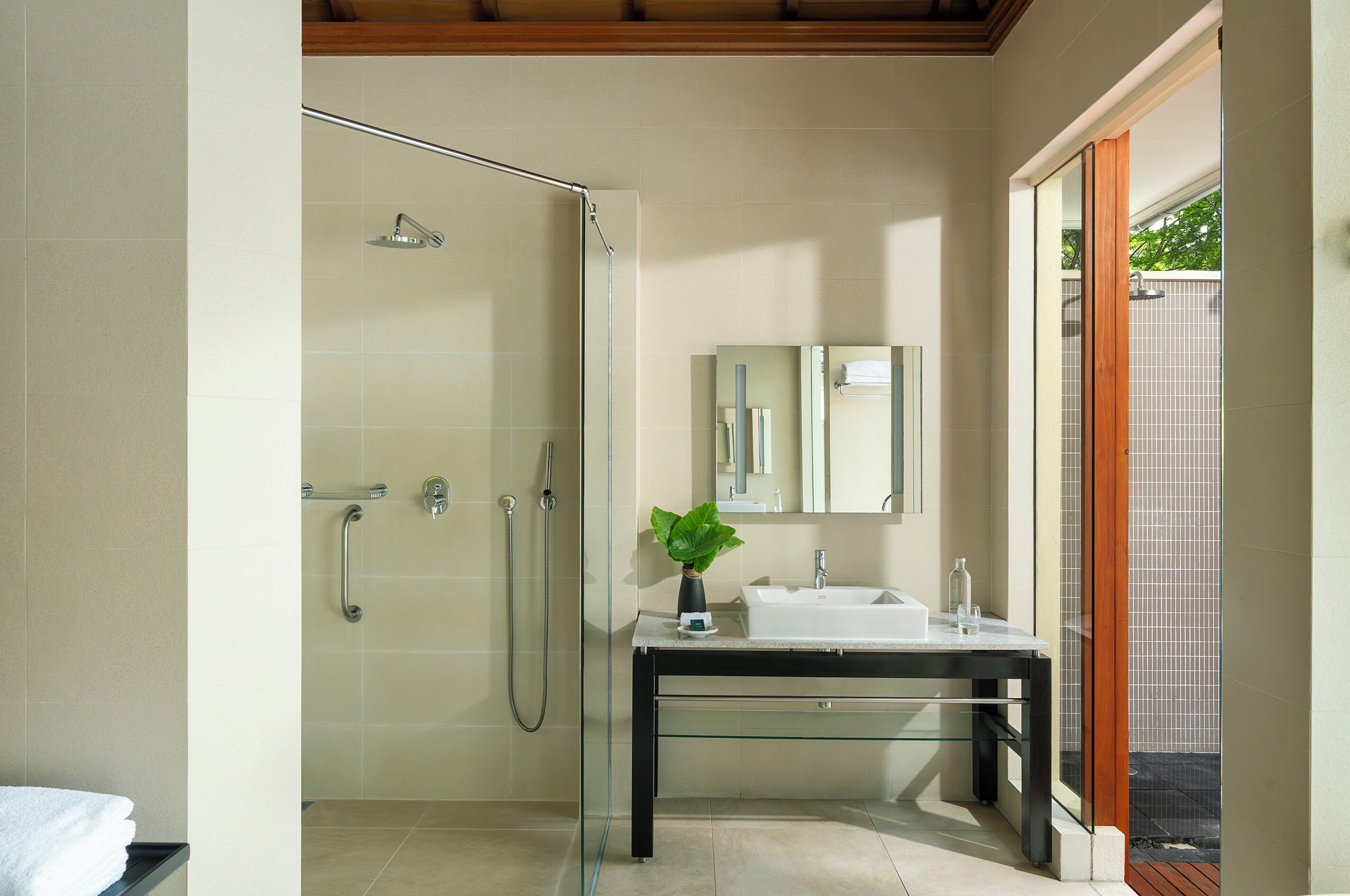 A modern bathroom with a glass shower enclosure, a sink with a mirror, and a potted plant.