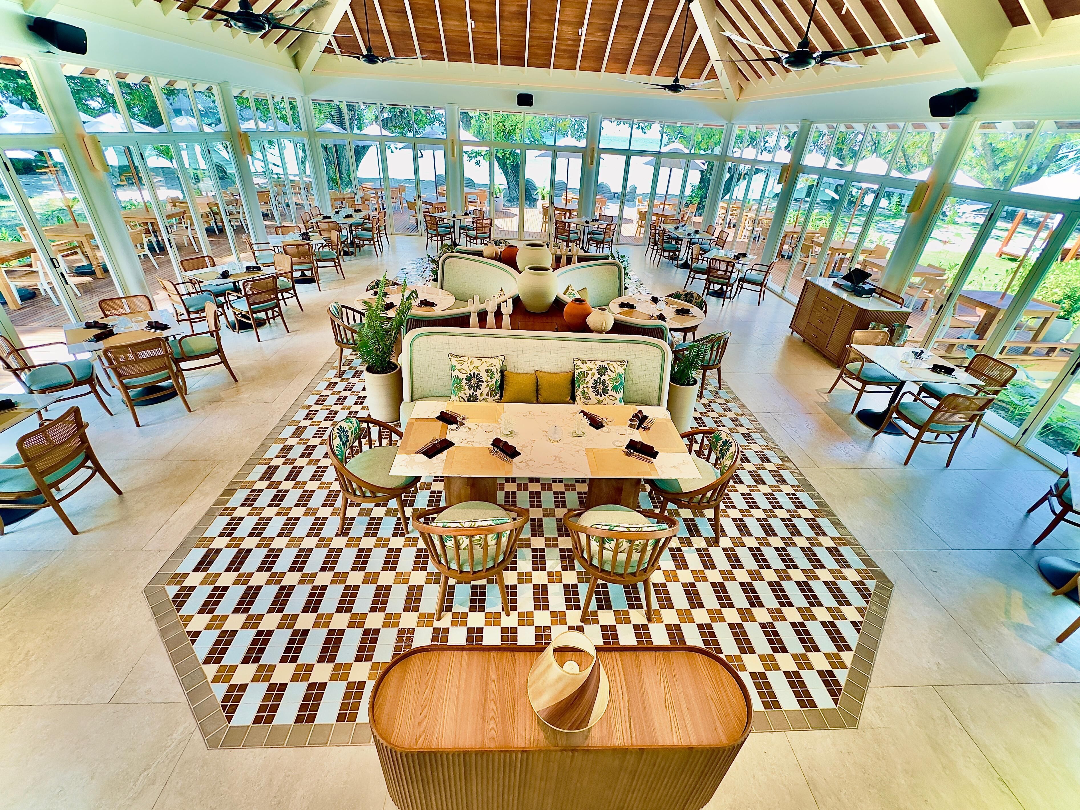 A spacious indoor dining area with multiple tables and chairs, large windows, and a ceiling fan.