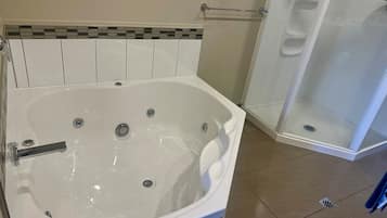 A bathroom with a large bathtub, a shower area, and a tiled floor.