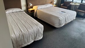 A hotel room with two beds, a small table, and a chair.