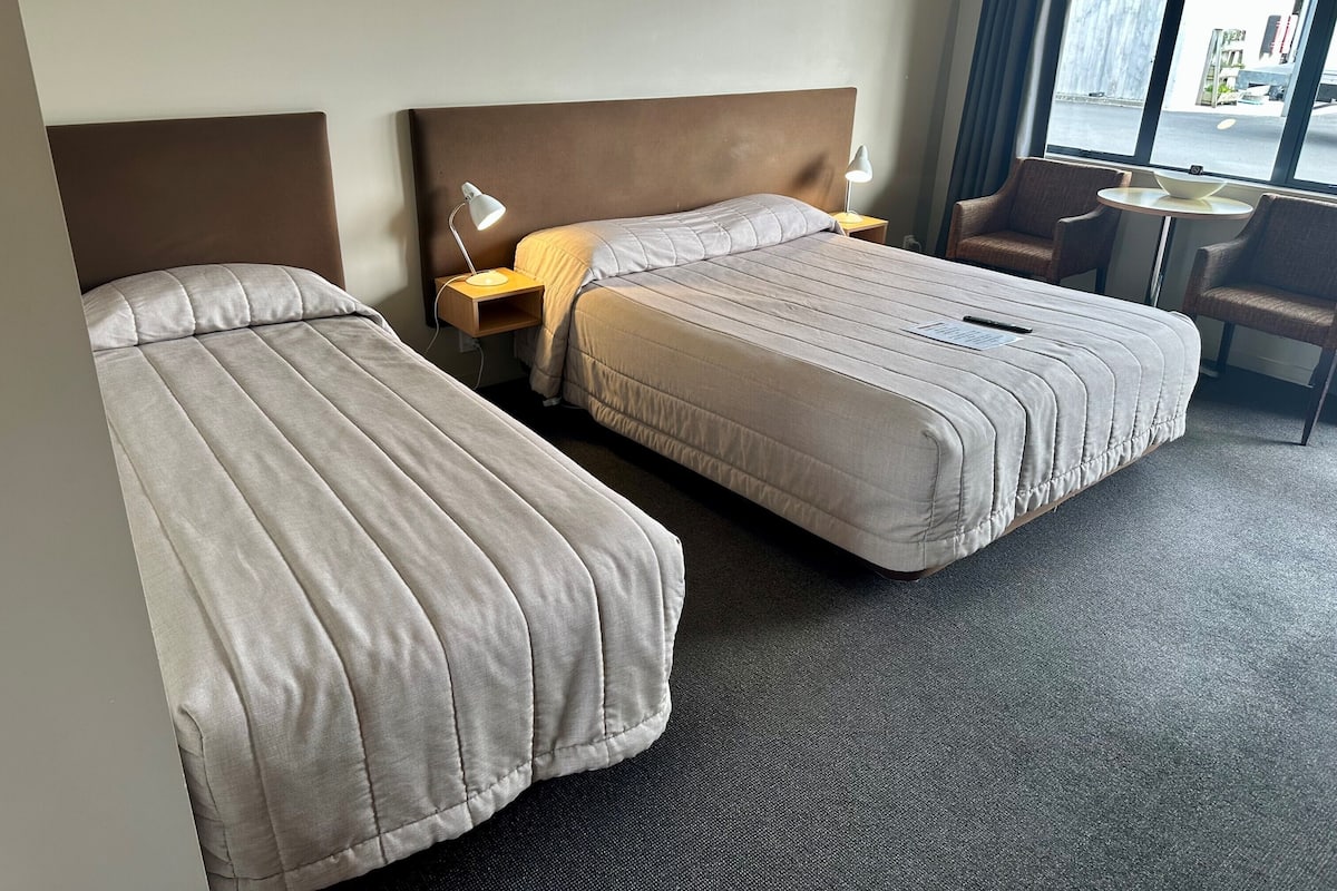 A hotel room with two beds, a small table, and a chair.
