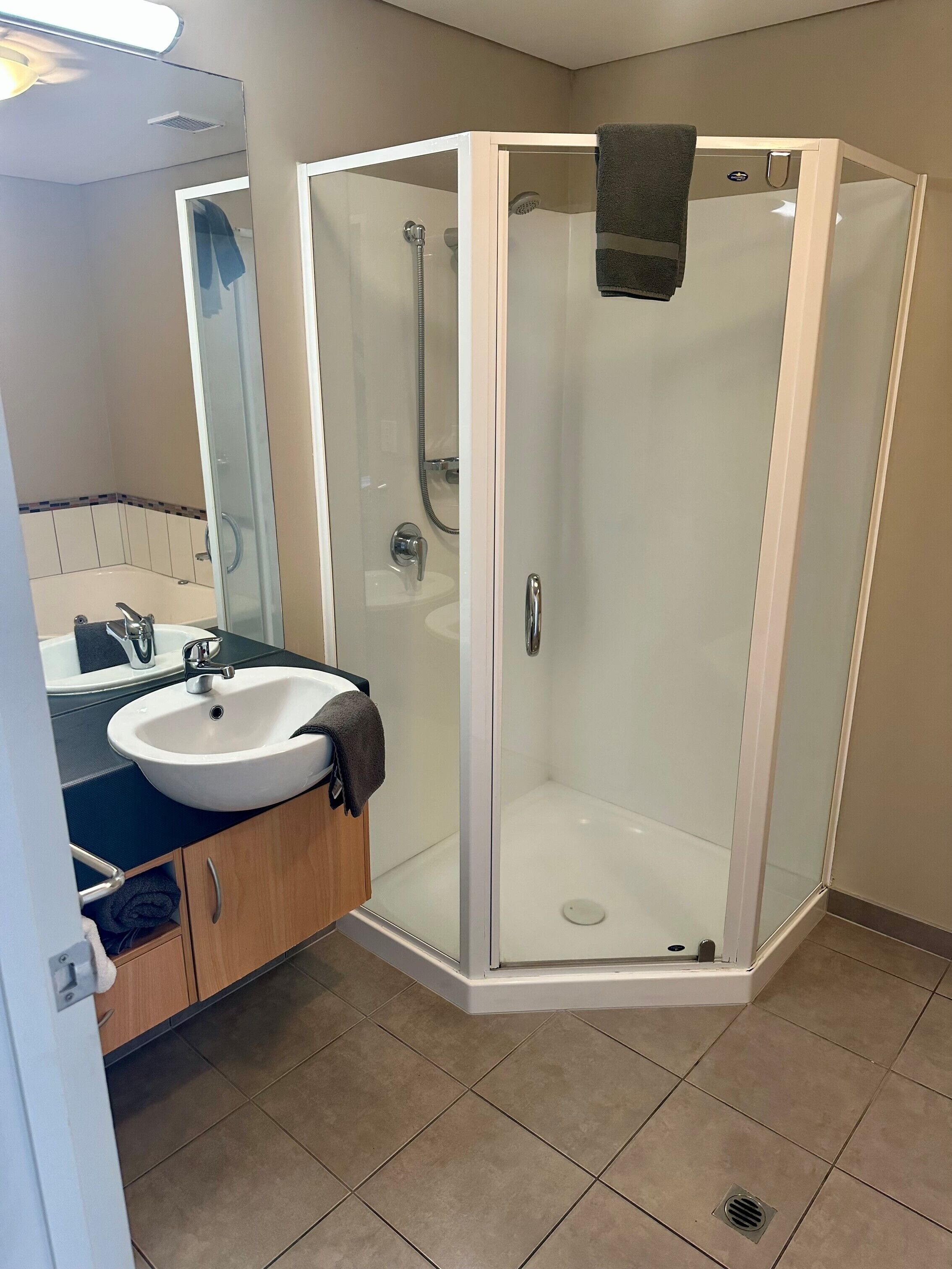 Un baño moderno con ducha de vidrio, lavamanos con toalla y espejo.