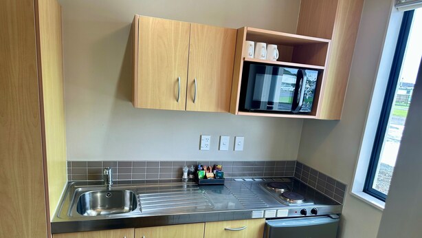 A compact kitchen with wooden cabinets, a stainless steel sink, a microwave, and a built-in oven.