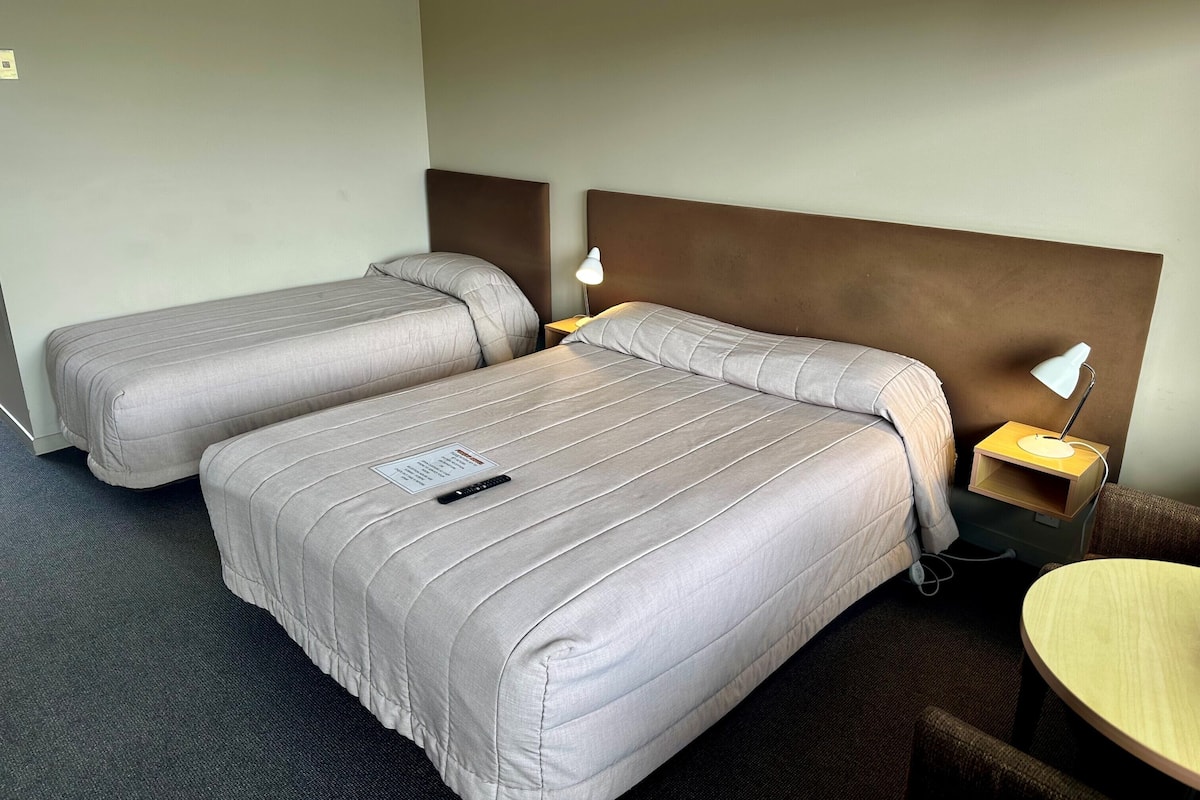 A hotel room with two beds, a desk, and a chair.