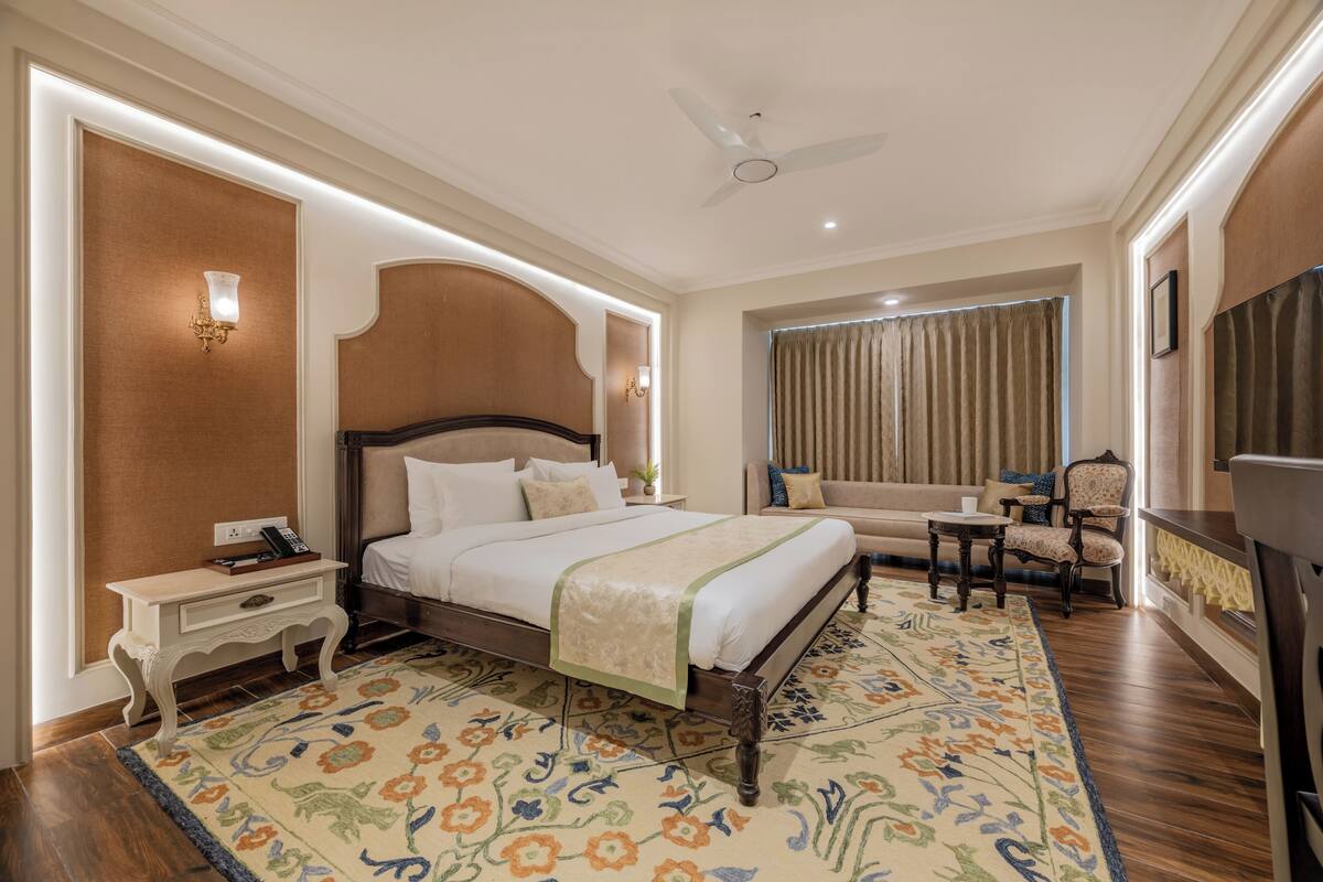 A hotel room with a large bed, a bedside table, a chair, a sofa, and a television.