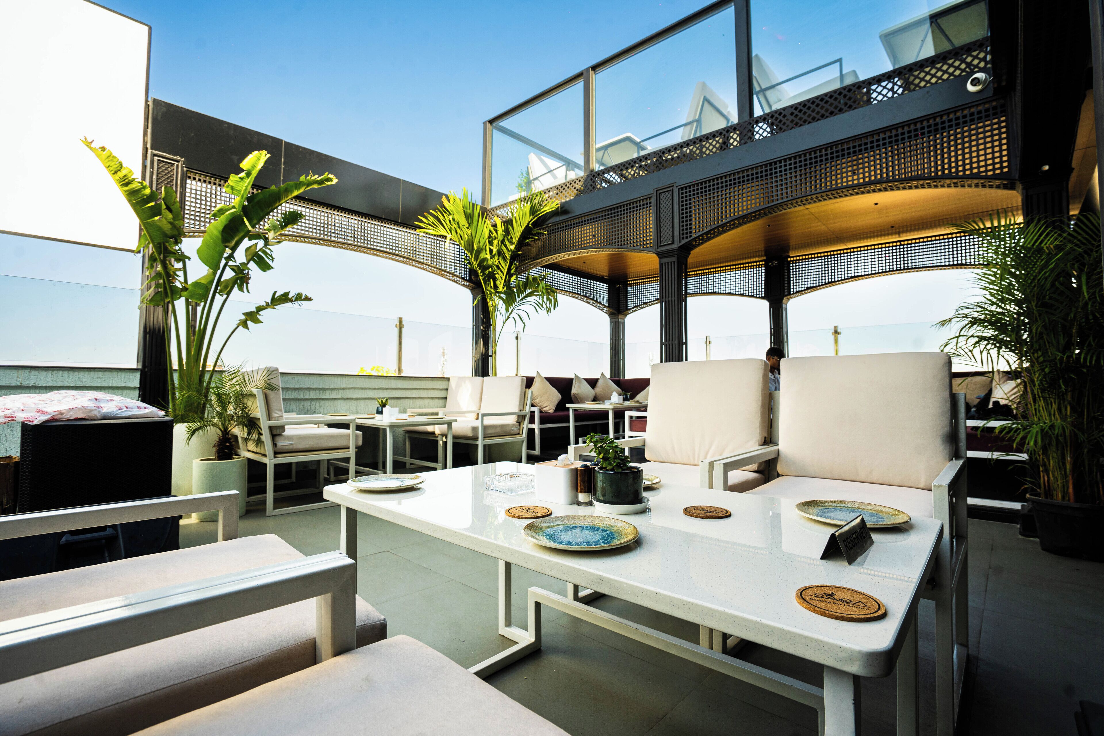 Een dakterras met buitenmeubilair, een glazen balustrade en potplanten.