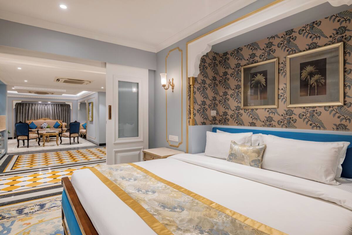 A hotel room with a large bed, a dining area with a table and chairs, and a patterned wall.