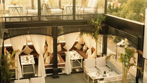 Un restaurante en la azotea con terraza, que incluye sofás y mesas, y vistas panorámicas de la ciudad.