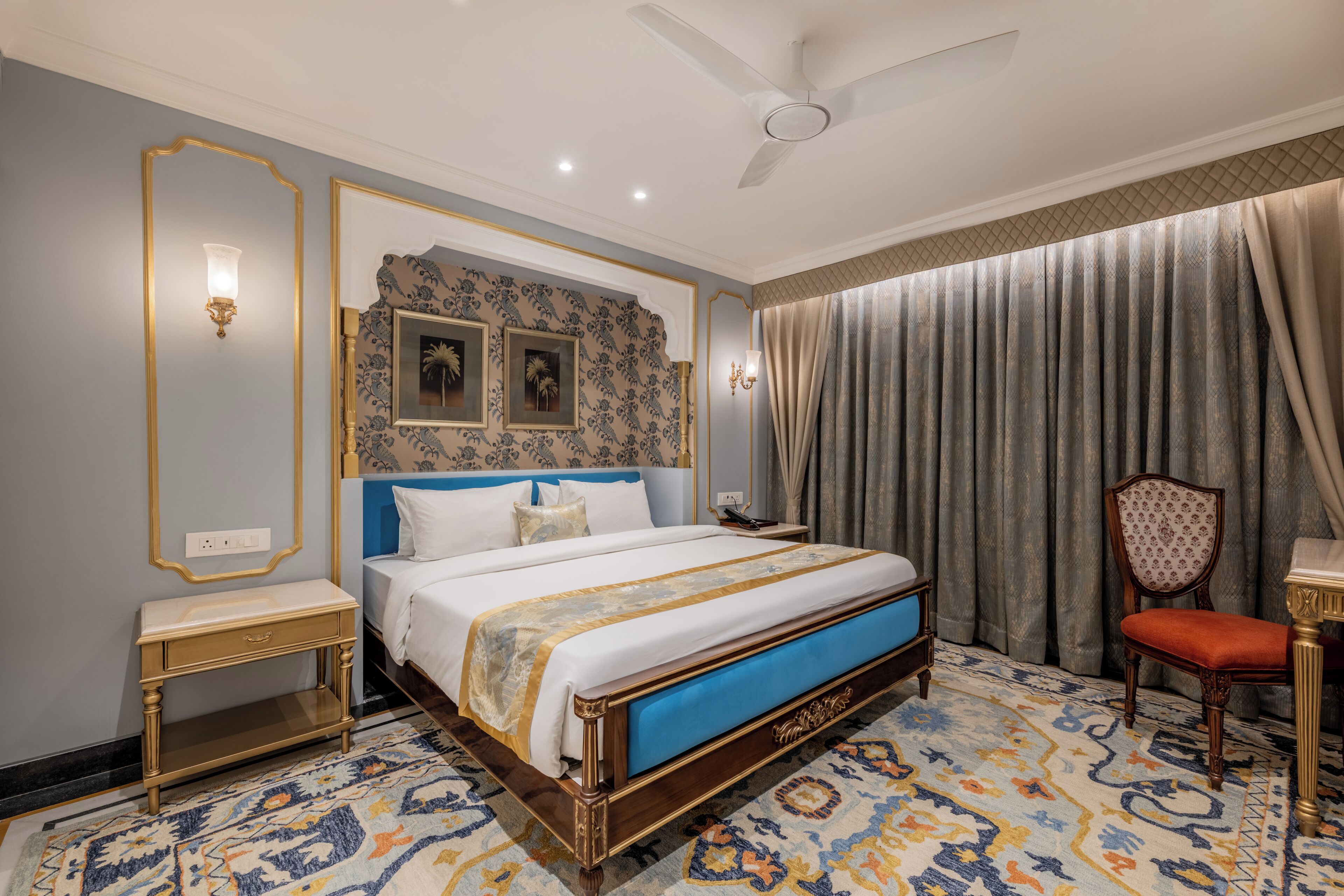 A bedroom with a large bed, a nightstand, a chair, a desk, and a ceiling fan.