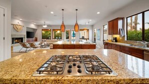A spacious kitchen with a central island, overhead pendant lighting, and a large window offering a view of the outdoors. - Indio Estate | Pool, Putting Green, Sleeps 12 (Indio)