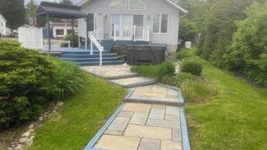 Ein Haus mit einer überdachten Veranda, einem Steinweg, der zur Haustür führt, und einem kleinen Garten mit Sträuchern und einer Rasenfläche.