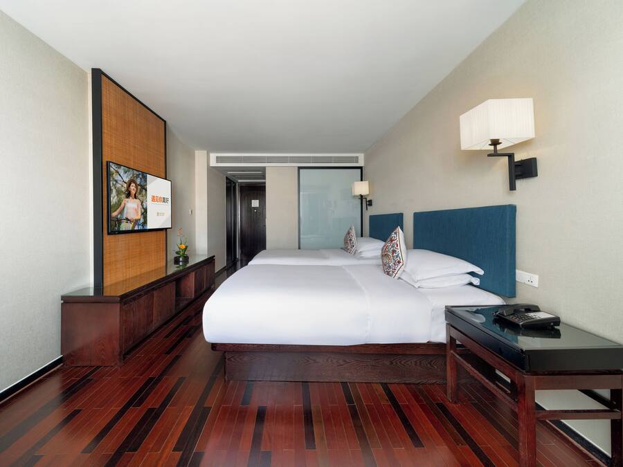 A hotel room with a large bed, a bedside table with a lamp, a wooden floor, and a wall-mounted TV.