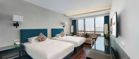 A hotel room with two beds, a sofa, a TV, and a large window offering a city view.
