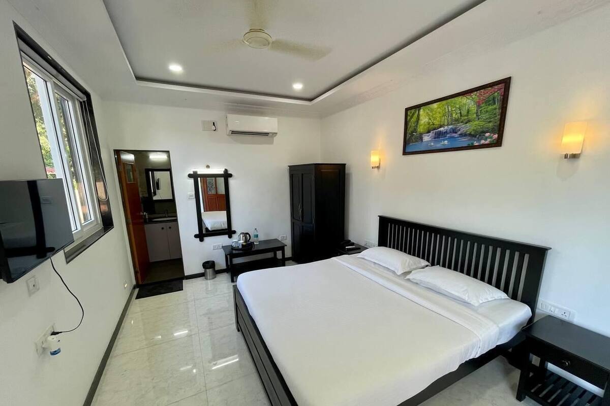 Una habitación de hotel con cama, televisión, escritorio, silla, armario y un cuadro en la pared.