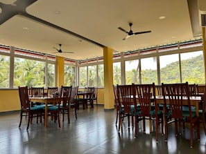 A dining area with tables and chairs, large windows, ceiling fans, and a view of palm trees. - Palm Paradise Resort (Querim)