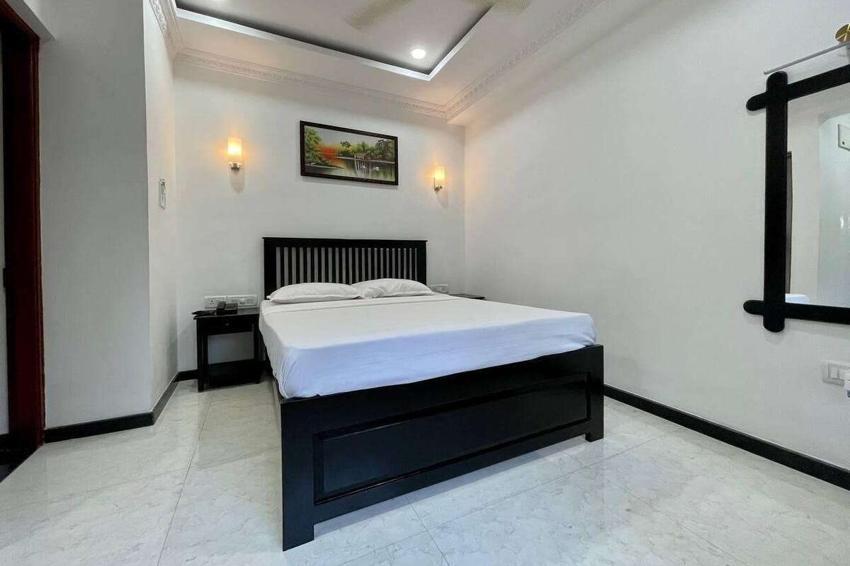 Un dormitorio con cama, mesita de noche, lámpara de pared, ventilador de techo y un cuadro en la pared.