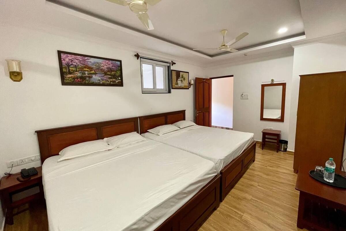 Habitación de hotel con cama doble, cabecera de madera, mesita de noche con teléfono, mesilla con lámpara, espejo y ventilador de techo.