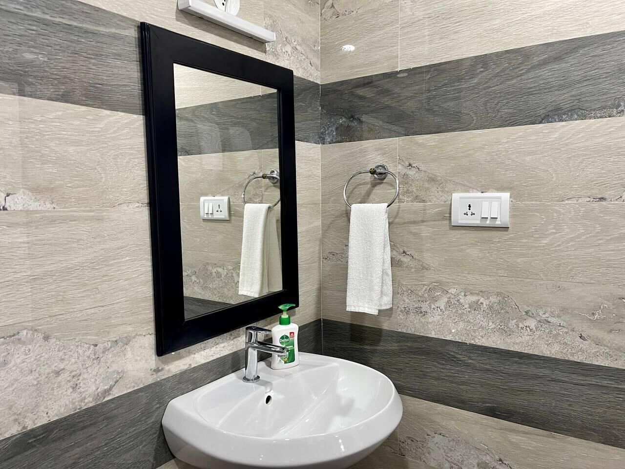 A bathroom with a white sink, a black-framed mirror, and a towel rack.