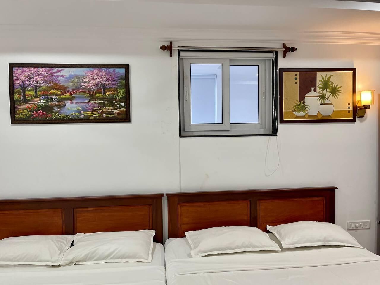Un lit double avec une tête de lit en bois, une fenêtre donnant sur un beau paysage et deux tableaux accrochés au mur.
