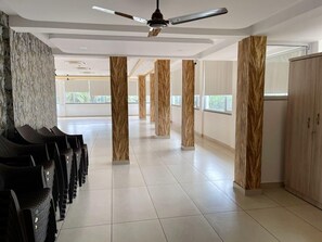 A hotel lobby with a row of black chairs, a ceiling fan, and tall wooden pillars. - Palm Paradise Resort (Querim)