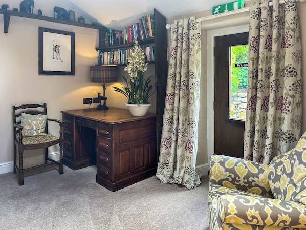 A room with a wooden desk, a chair, a bookshelf, a potted plant, and a window with curtains.