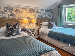 A bedroom with two beds, a nightstand with lamps, and a window with curtains. - Gillhead Farm Cottage (Matterdale End)