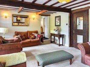 A cozy living room with a brown leather sofa, a green ottoman, and a wooden coffee table. - Gillhead Farm Cottage (Matterdale End)