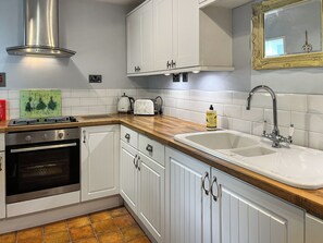 A kitchen with white cabinets, a stainless steel range hood, a double sink, and a wooden countertop.