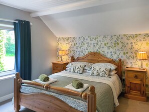 A bedroom with a wooden bed, floral wallpaper, two bedside tables with lamps, and a window with curtains. - Gillhead Farm Cottage (Matterdale End)