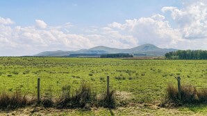 A wide-open field with a mountain range in the distance, a clear sky, and a wooden fence in the foreground. - Gillhead Farm Cottage (Matterdale End)