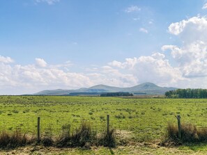 A wide-open field with a mountain range in the distance, a clear sky, and a wooden fence in the foreground. - Gillhead Farm Cottage (Matterdale End)